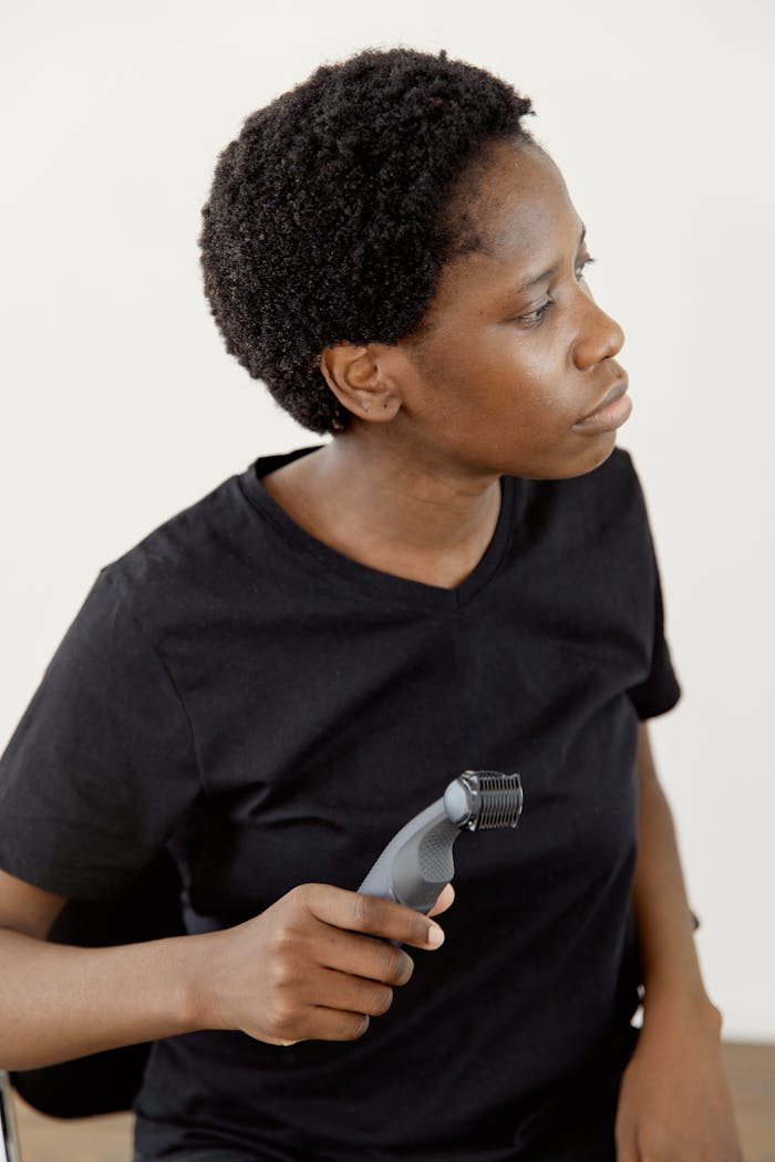 Black woman with afro holding a razor, wearing a black shirt indoors, looking thoughtful.